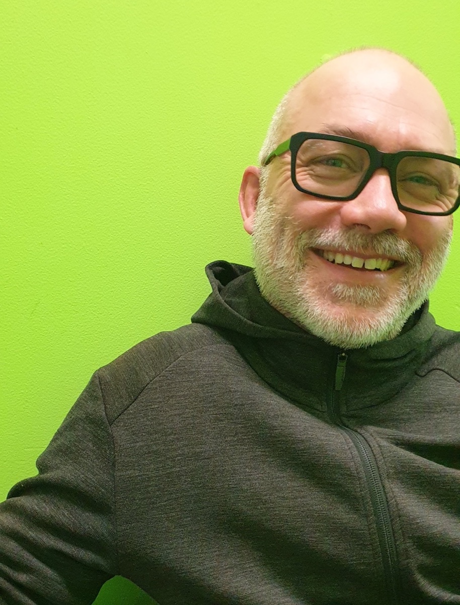 Photo of Gary Peters smiling while sitting at a table against a bright green wall.